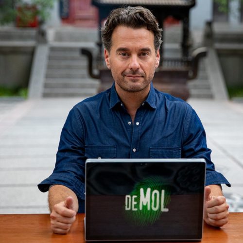 Presentatotor 'Wie is de mol?' achter laptop met logo WIDM.