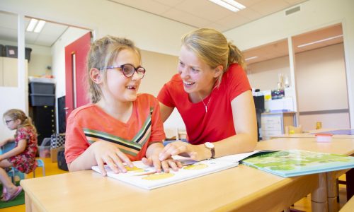 Leerkracht helpt leerling met braille in boek