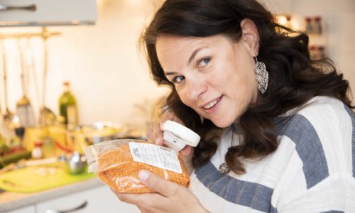 Annemiek in de keuken terwijl zij met een vergrootglas een verpakking leest