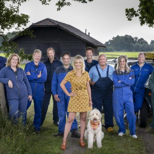 Groepsfoto van alle boeren die dit seizoen meedoen aan Boer zoekt vrouw. De boeren dragen blauwe overalls. In het midden staat Yvon Jaspers in een gele jurk met haar hond.