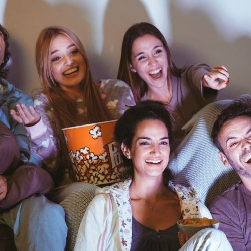 Groep van vijf vrienden kijken TV en lachen samen.