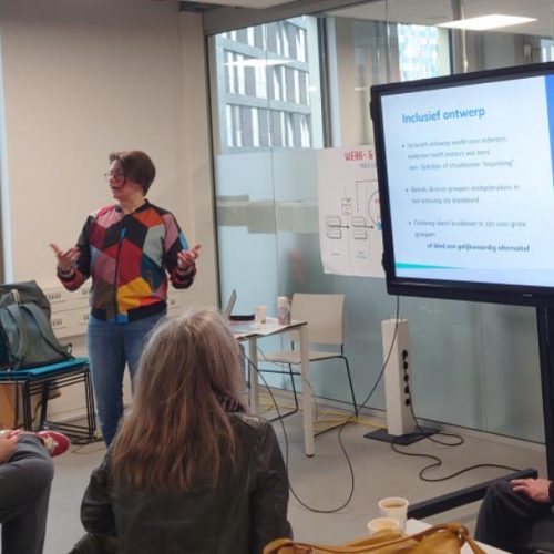 Studenten in een klaslokaal luisteren naar ervaringsdeskundige Severine Kas. Op een beeldscherm een presentatie over Digitale Toegankelijkheid.