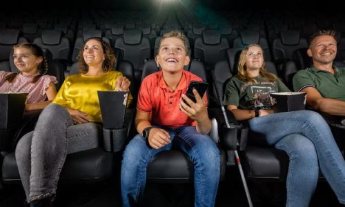 Jongen met visuele beperking kijkt in de bioscoop een film met audiodescriptie, samen met zijn familie.