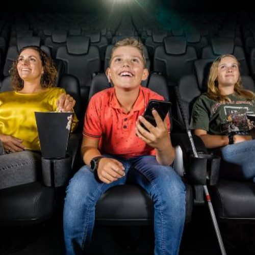 Jongen met visuele beperking kijkt in de bioscoop een film met audiodescriptie, samen met zijn familie.
