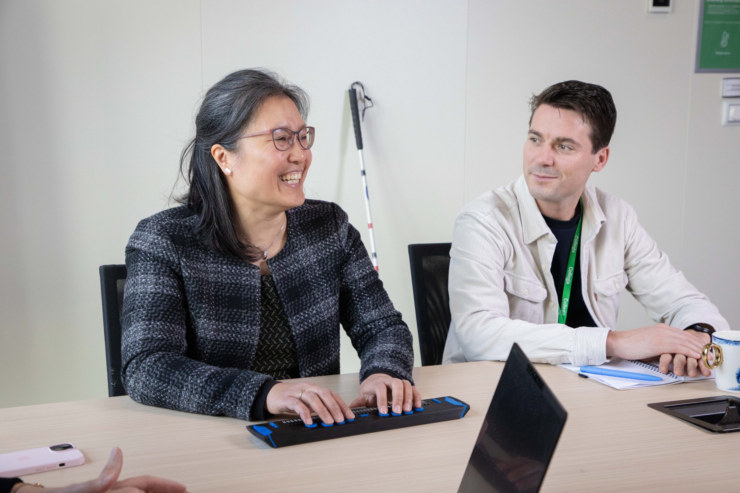 Slechtziende vrouw op kantoor met een collega. De vrouw gebruikt een braille leesregel.
