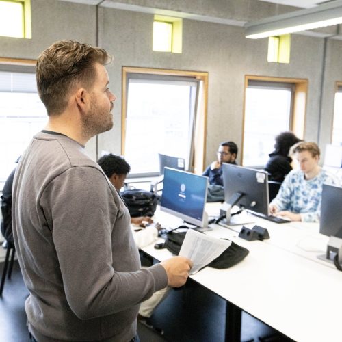 Docent voor een groep studenten. De studenten zitten achter beeldschermen.