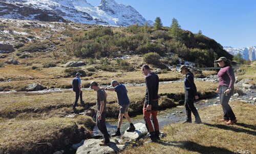 Simon steekt samen met een buddy een beekje over in de Alpen. Er zijn nog 3 wandelaars.